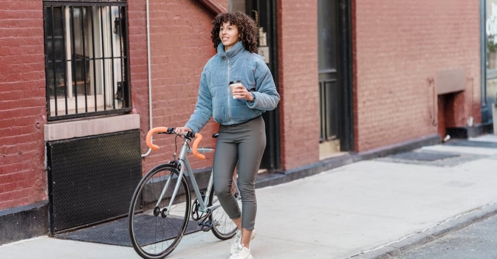 Woman walking her bicycle on the street while holding a takeaway coffee cup.